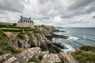 Vue grand angle d'un manoir breton en pierre avec toit ardoise surplombant des falaises atlantiques, illustrant le marché immobilier de luxe en Bretagne