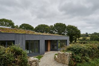 Maison passive moderne en Bretagne avec bardage en fibrociment et fenêtres triple vitrage intégrées dans un paysage bocager breton