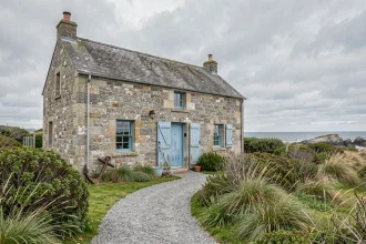 Maison de pêcheur en pierre de granit à vendre en Bretagne avec volets bleus et végétation côtière