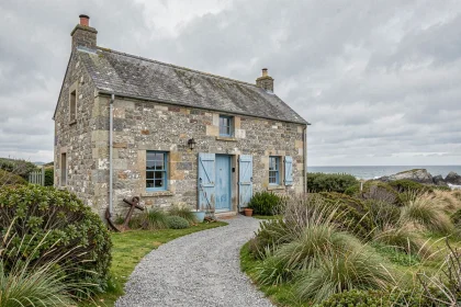 Maison de pêcheur en pierre de granit à vendre en Bretagne avec volets bleus et végétation côtière